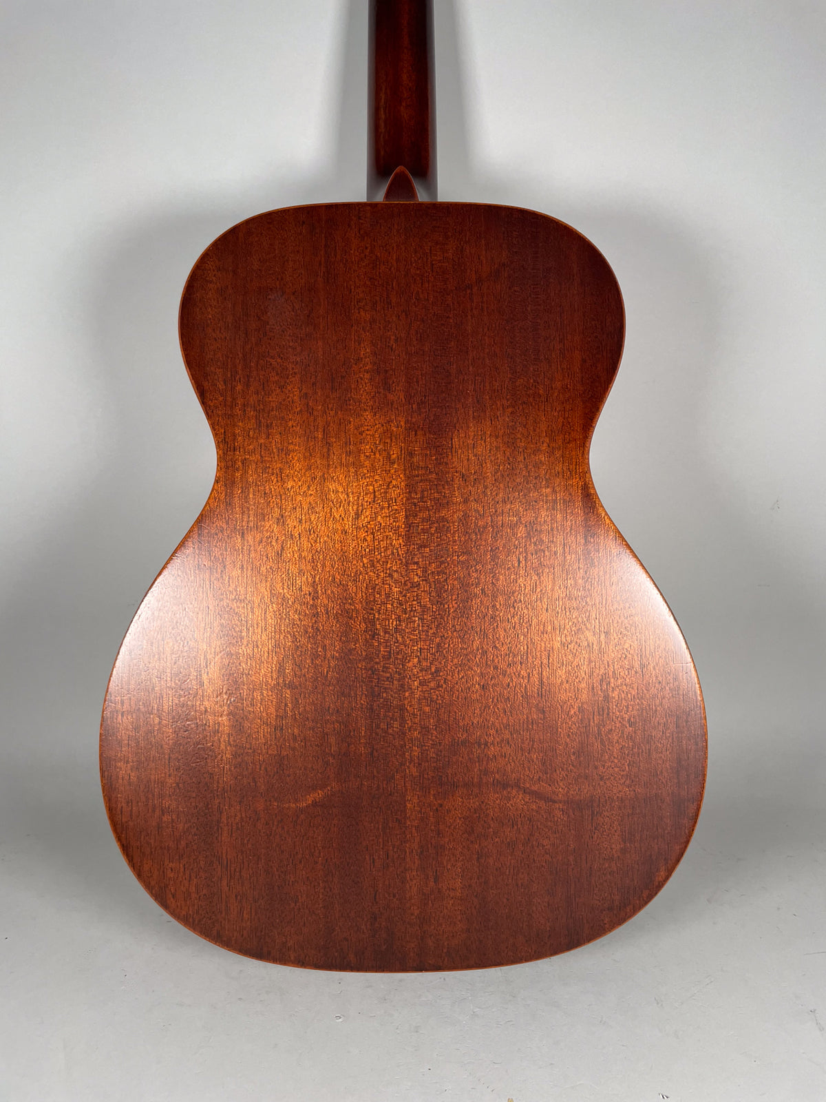 The back of a reddish-brown acoustic guitar, showing the full body and part of the neck, with a few light scuffs on the lower bout.
