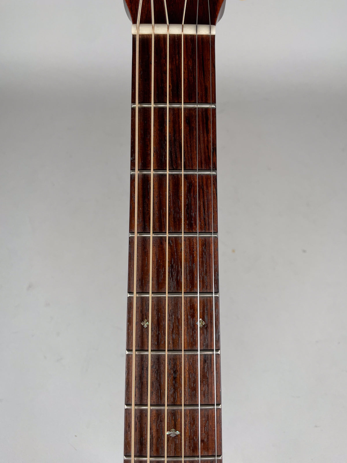 A close-up, top-down view of the dark brown fretboard with six strings, showing diamond-shaped fret markers on the 5th, 7th, and 9th frets.