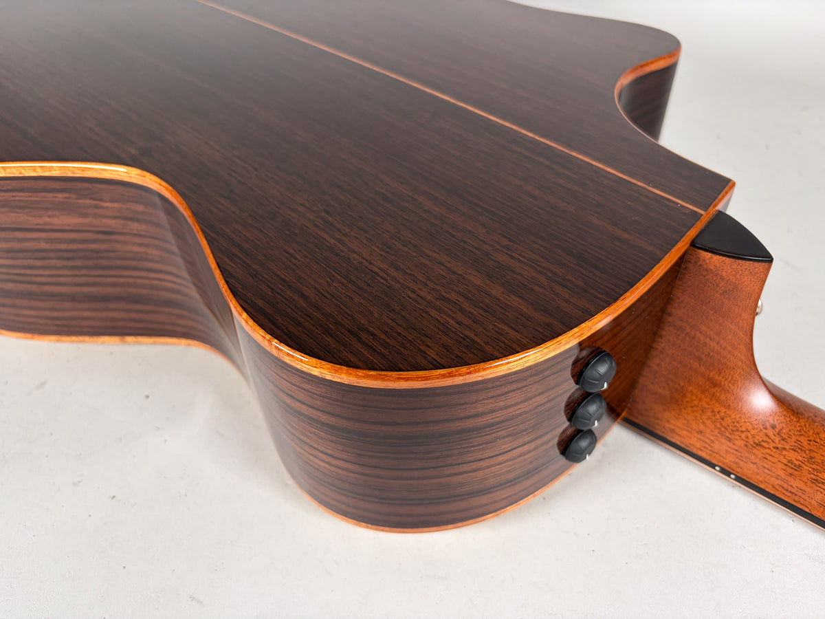 The guitar's dark brown back and side are visible, with three black control knobs on the lower bout and a light brown neck heel.