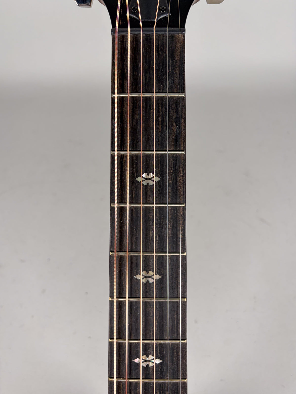 Close-up of a dark wood guitar fretboard with three mother-of-pearl "Reflections" inlay markers and six strings.