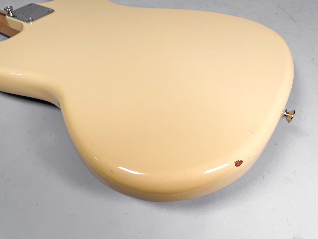 The back of a cream-colored Mustang guitar body, showing a chrome neck plate and a chip in the finish near the lower strap button.