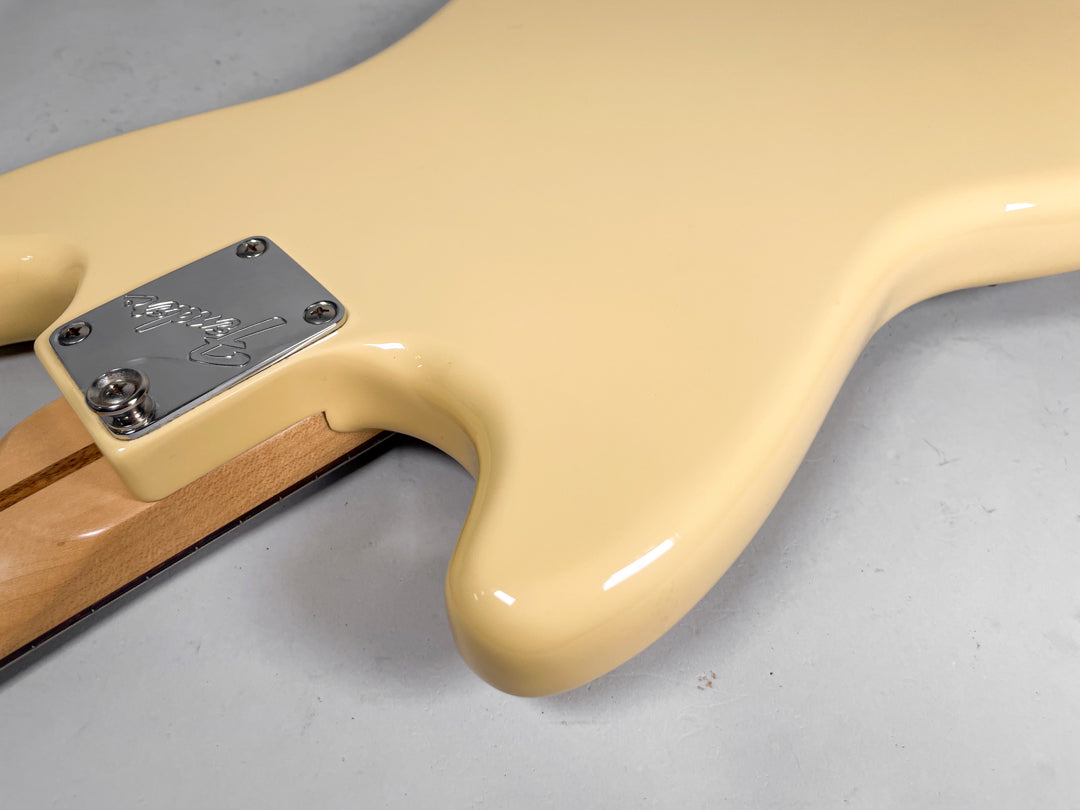 Close-up of the guitar's creamy yellow body, showing the chrome neck plate with an engraved logo and a strap button.