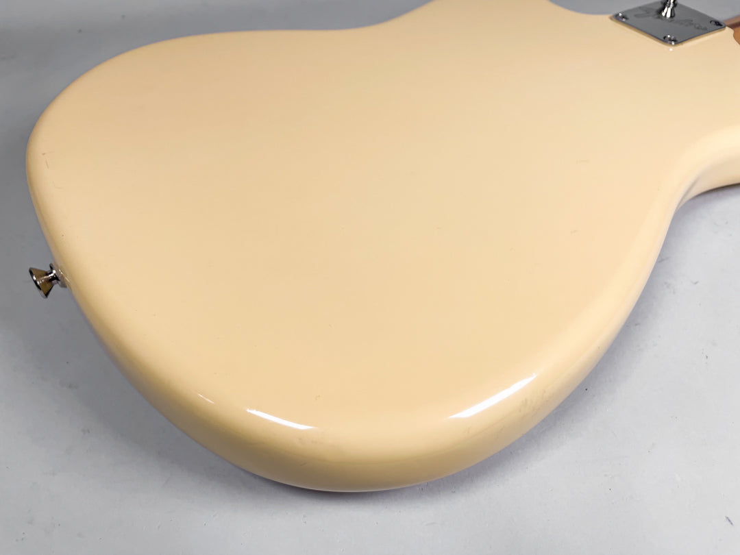 The back of a creamy yellow guitar body, angled from the lower bout to the neck plate, shows light scuffs near the strap button.