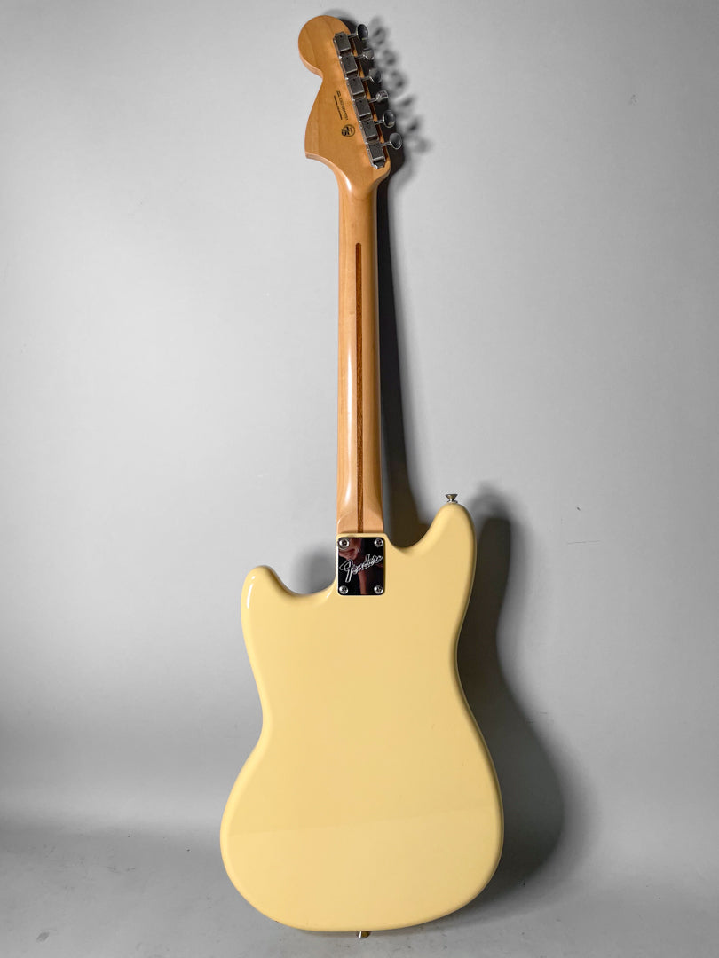 The back of a creamy yellow Mustang guitar, with a light wood neck and chrome tuning pegs and neck plate.