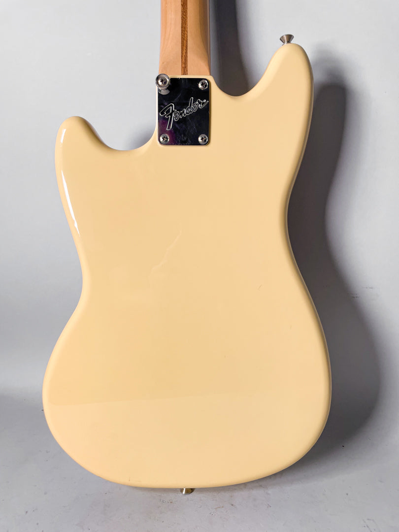 The back of a glossy cream Mustang guitar, showing the neck plate, strap buttons, and a faint scratch on the body.