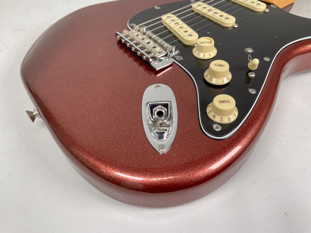 Close-up of the metallic copper Stratocaster body, showing the input jack, black pickguard, three cream knobs, and bridge.