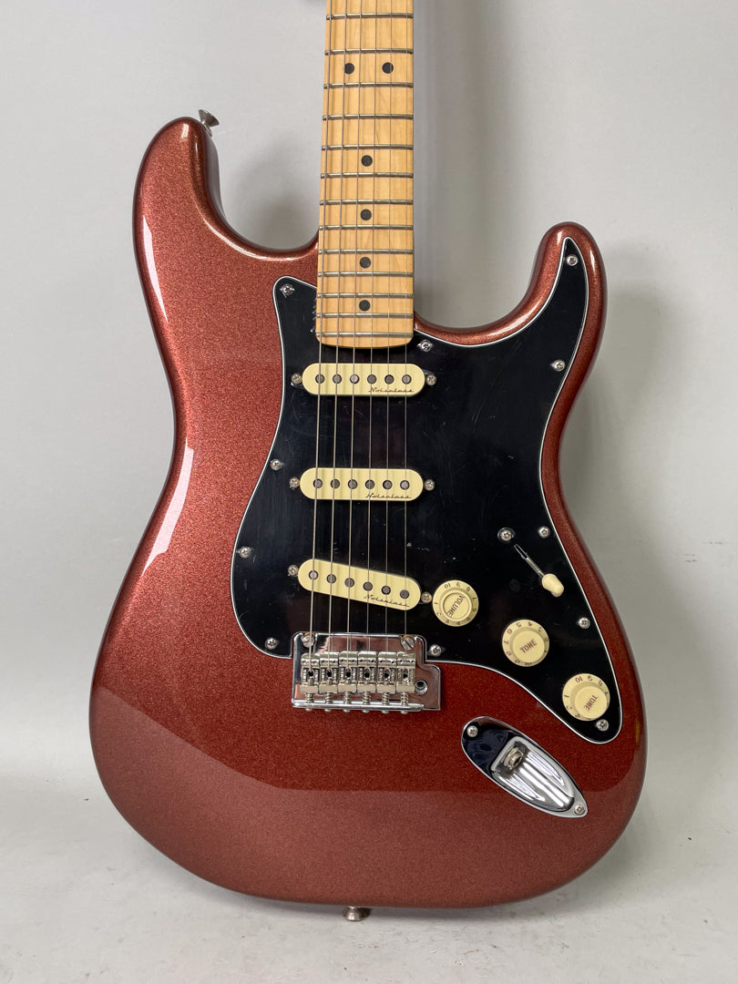 Full-frame shot of a metallic copper Stratocaster with a black pickguard, three cream single-coil pickups, and a maple fretboard.