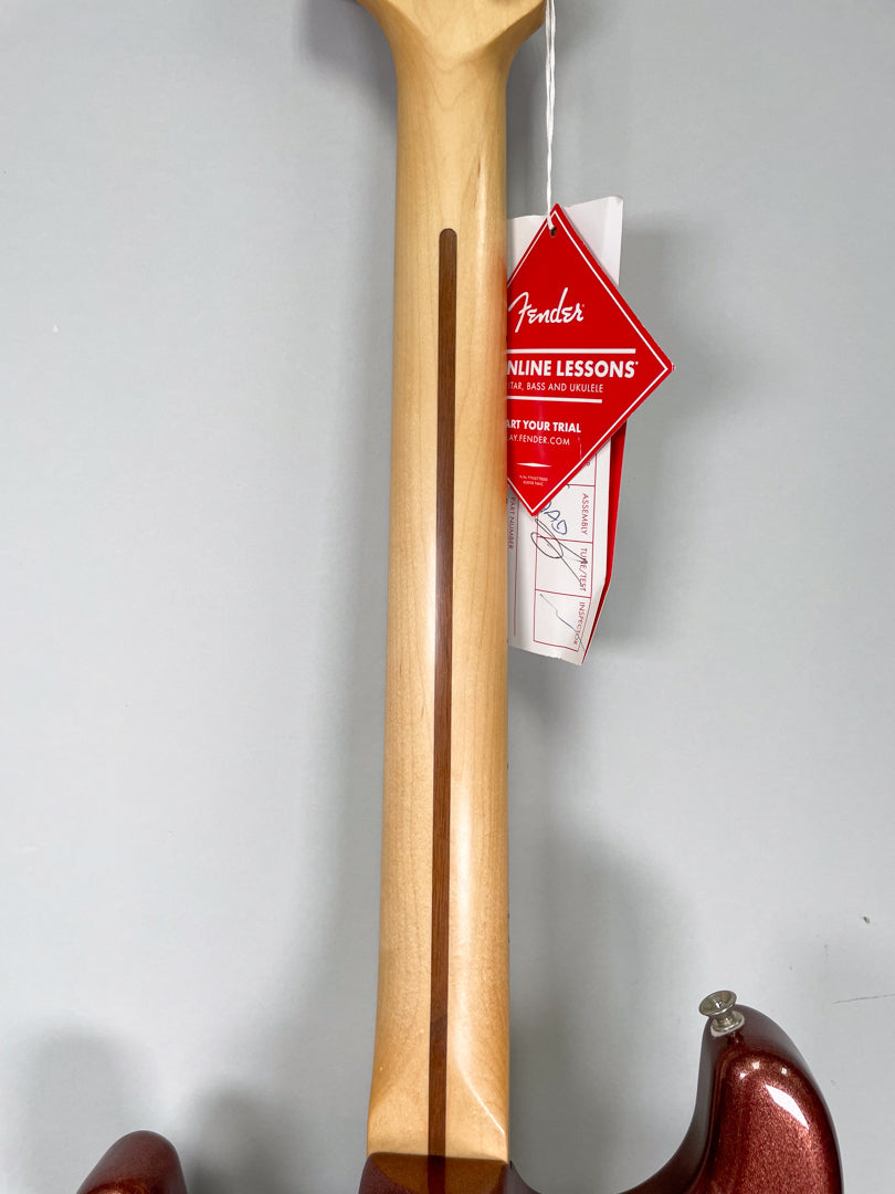 The guitar's maple neck and headstock are viewed from behind, with a dark wood stripe and a red Fender tag hanging from the tuners.
