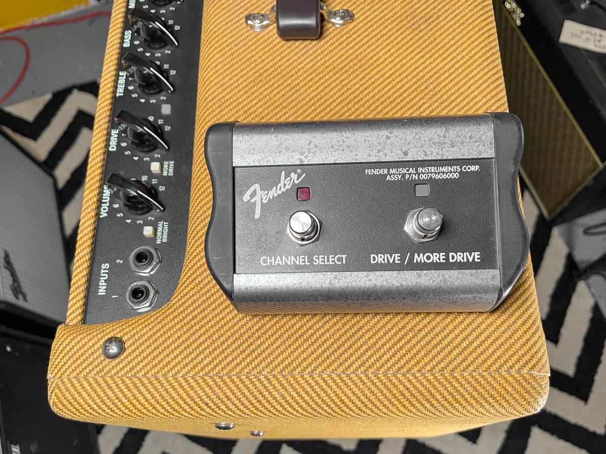 Overhead view of the tweed amp's top, showing the black control panel with knobs and a gray two-button footswitch.
