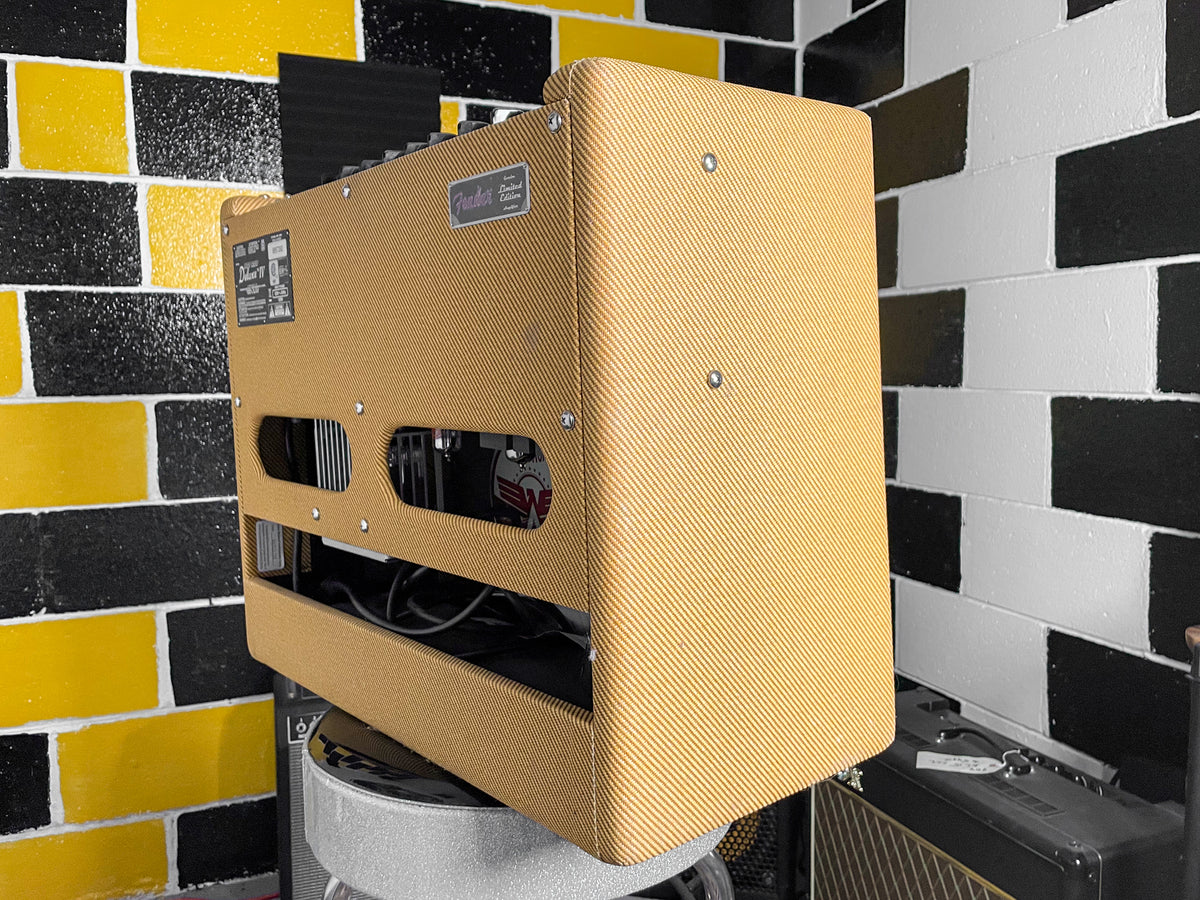 The tweed combo amp is angled right, showing its textured tan finish, two side vents, and a metal badge on the top.