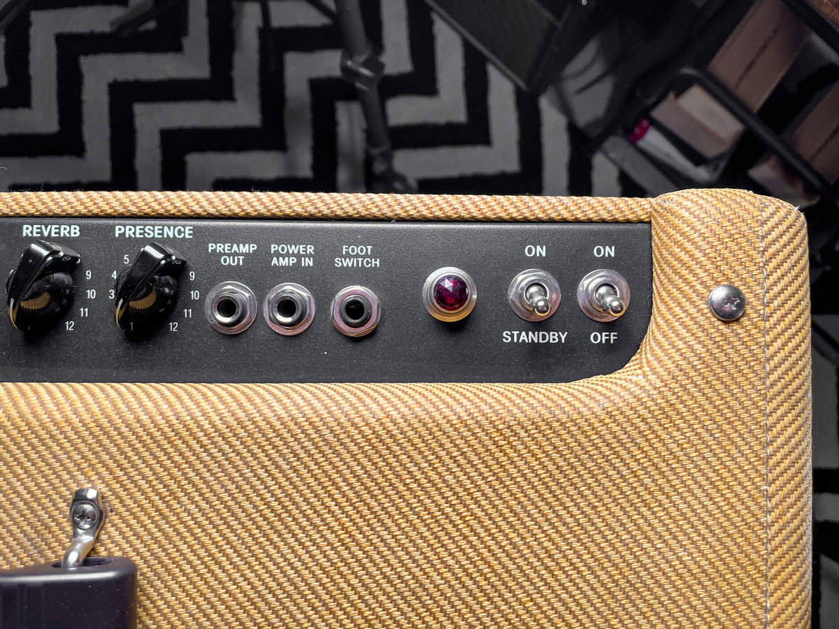 Close-up of the tweed amp's black control panel, showing two black knobs, three input jacks, a red jewel light, and two toggle switches.