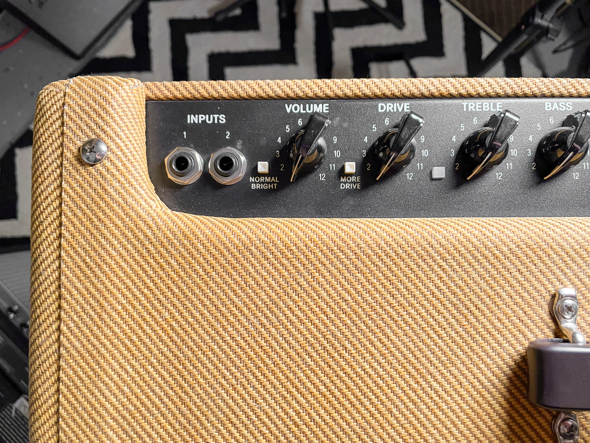 Close-up of the tweed amp's top left, showing the black control panel with inputs, Volume, Drive, Treble, and Bass knobs.