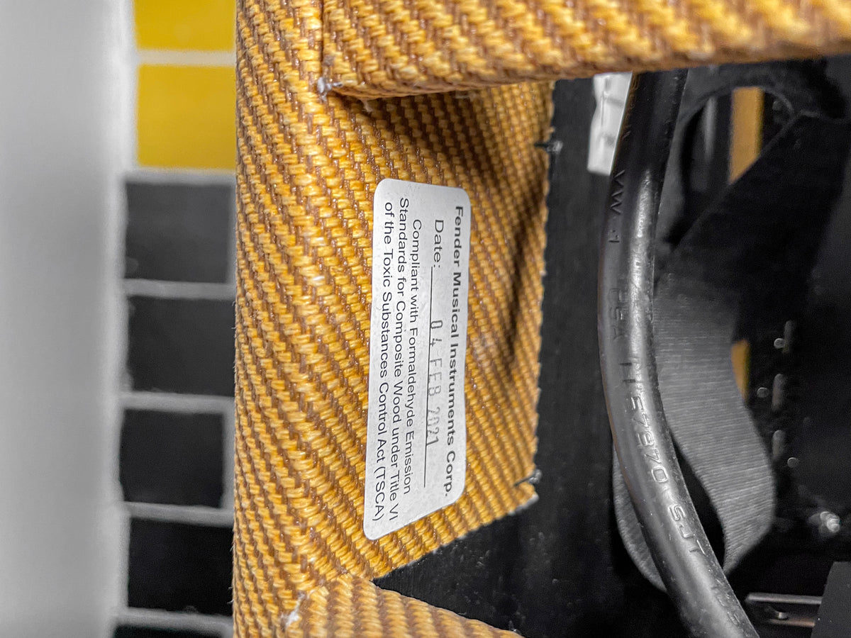 Close-up of the amp's tweed covering and a white label with black text, partially obscuring internal wiring and a black strap.