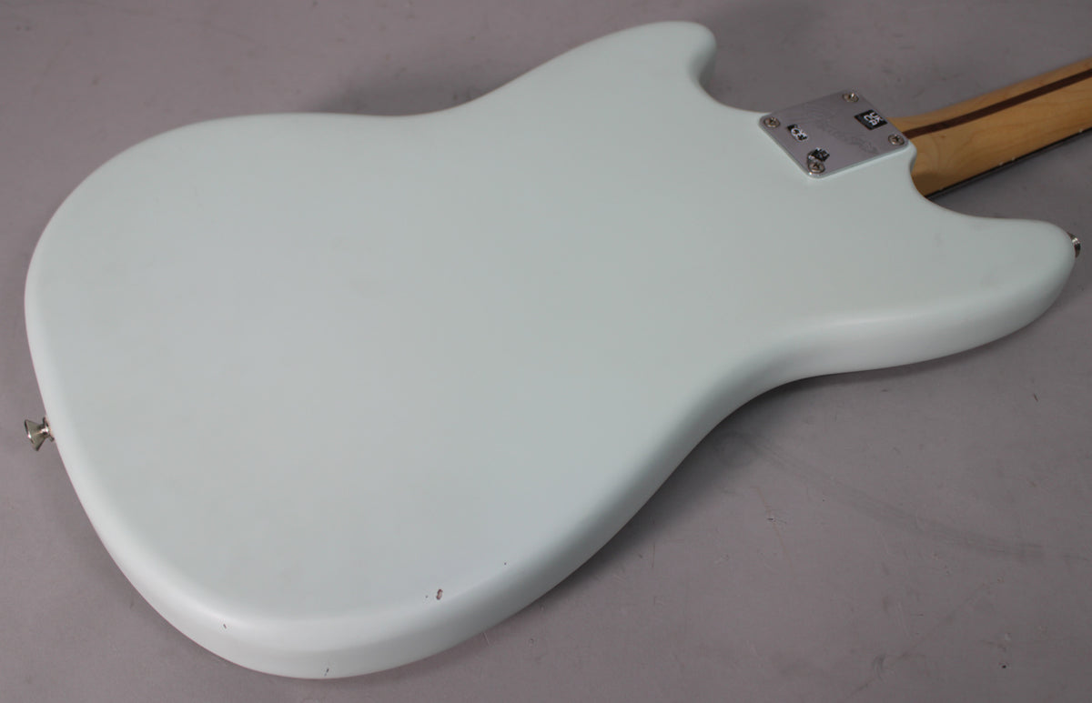 The back of a sonic blue Mustang guitar, showing the neck plate, strap button, and a few small dings on the lower edge.
