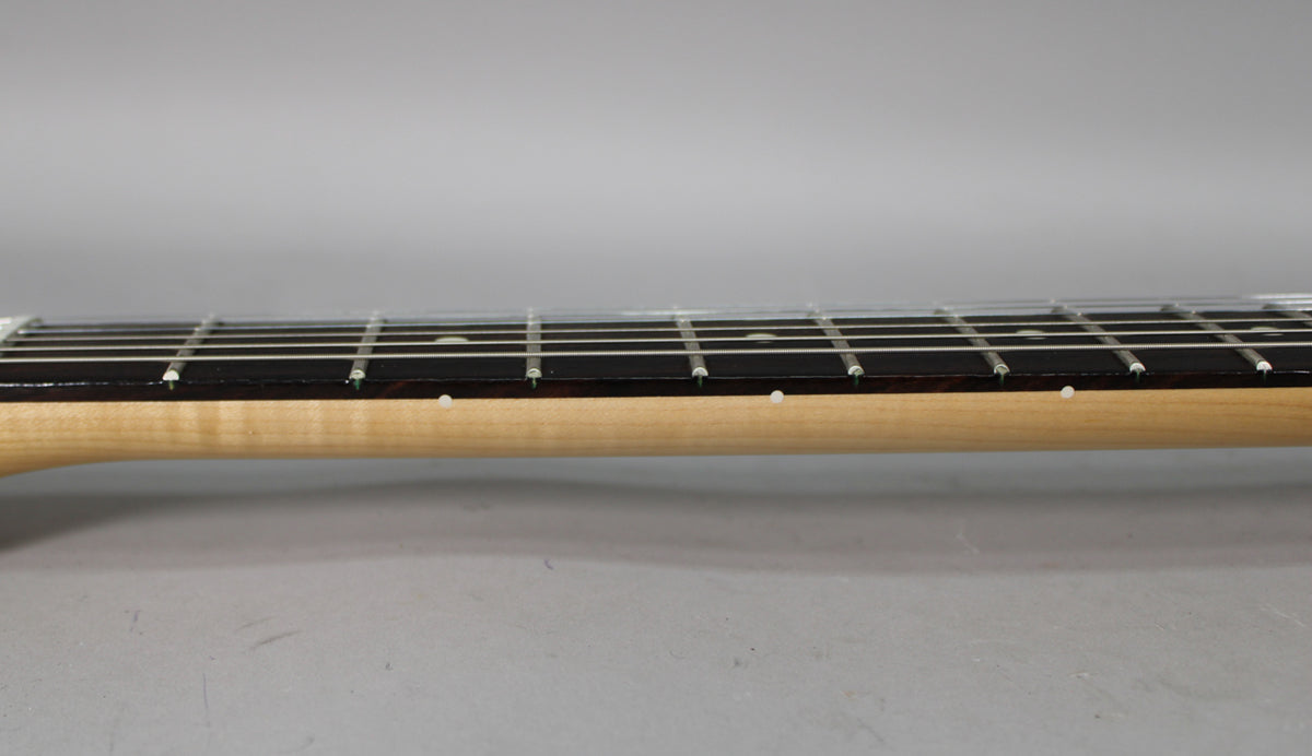 The guitar's light maple neck and dark fretboard are seen from the side, with white dot inlays visible on the neck.