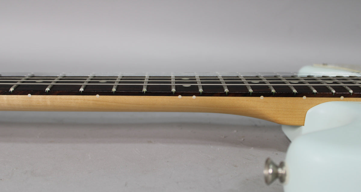 Close-up of the guitar's neck and fretboard from the side, showing the light maple neck, dark fretboard, and white dot inlays.