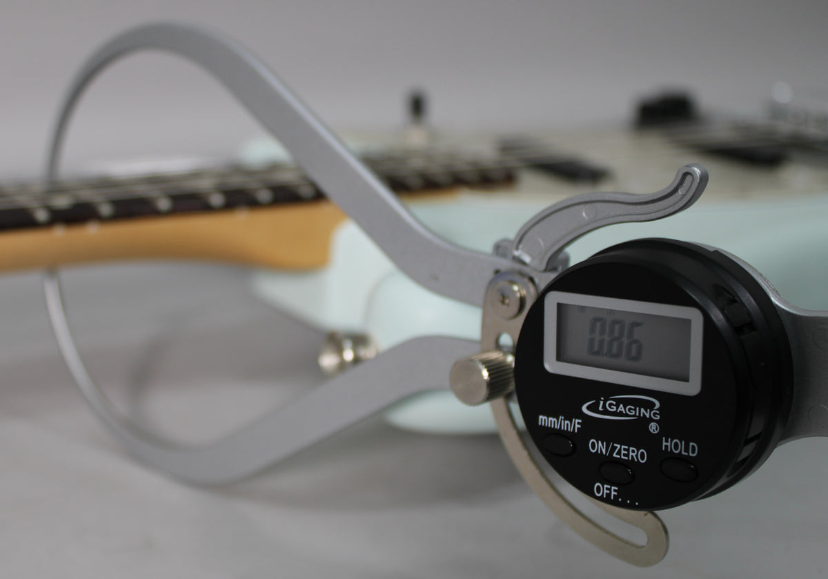 A digital caliper measures the fret height of the Sonic Blue Mustang, showing 0.86mm, with the neck and body out of focus.