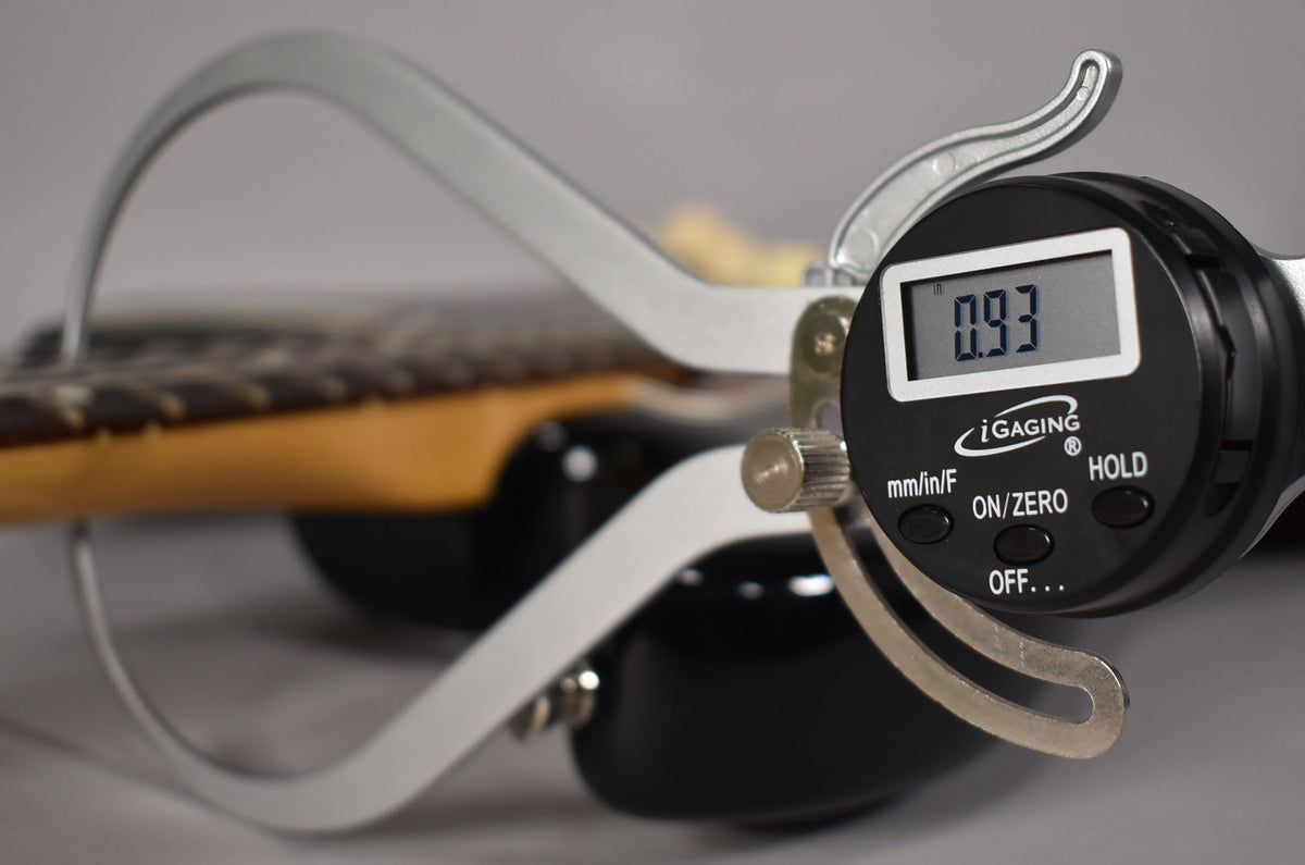 A digital caliper measures the string height at 0.93mm on the dark rosewood fretboard of the sunburst Stratocaster.