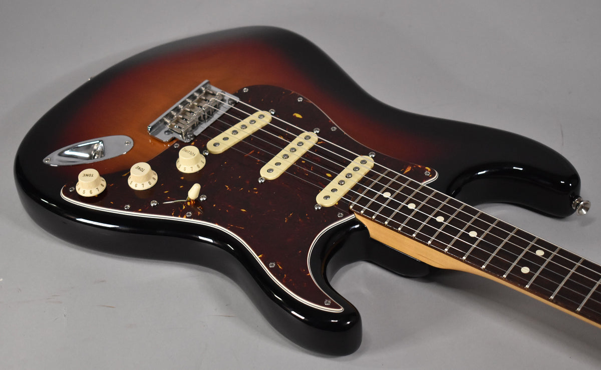 Sunburst Stratocaster, body angled from upper left, showing tortoise pickguard, three cream single-coil pickups, and chrome hardware.