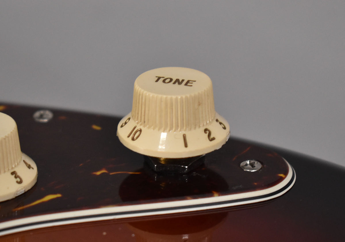 Close-up of the cream "TONE" knob with numbers 1-10 on a tortoiseshell pickguard, with a sunburst body visible below.