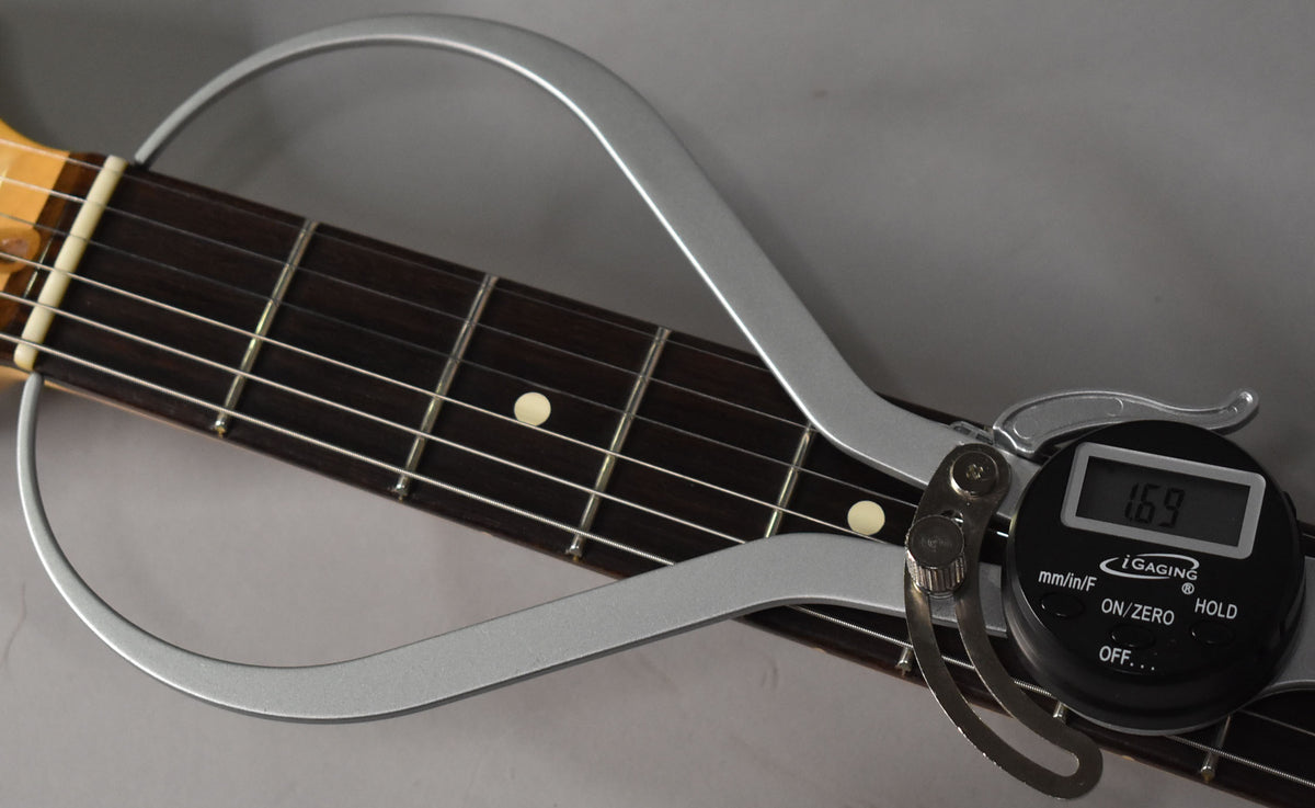 Close-up of the guitar's dark fretboard with light dot inlays, showing a silver digital caliper measuring the fret height at 1.69mm.