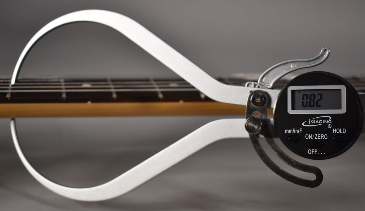 A digital caliper measures the fret height on the guitar's maple neck and dark fretboard, displaying "0.82".
