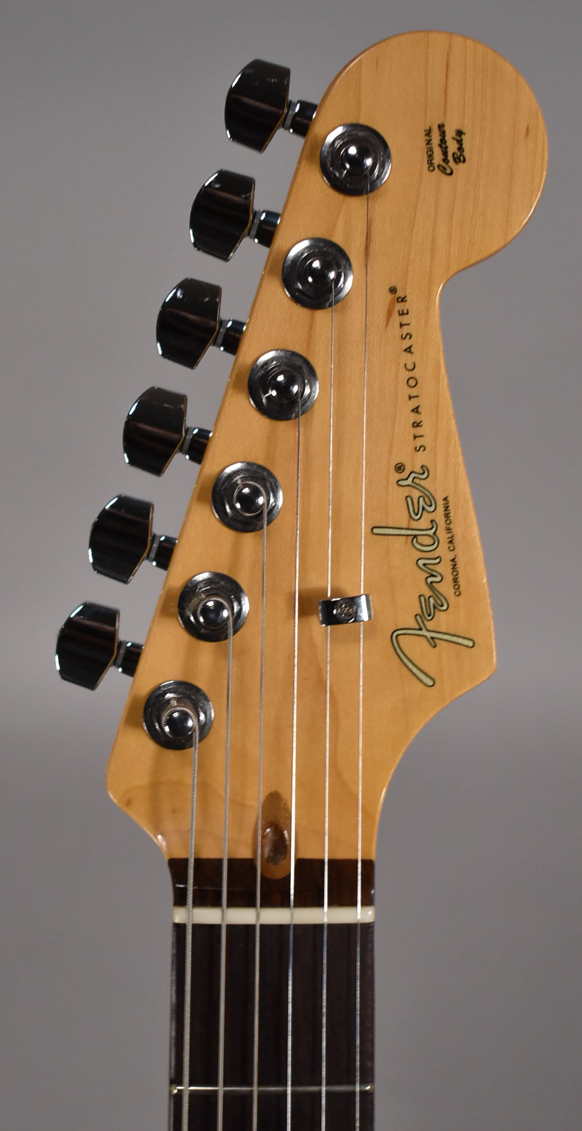 Close-up of the light maple headstock, angled slightly left, showing six chrome tuners, a string tree, and the dark fretboard.