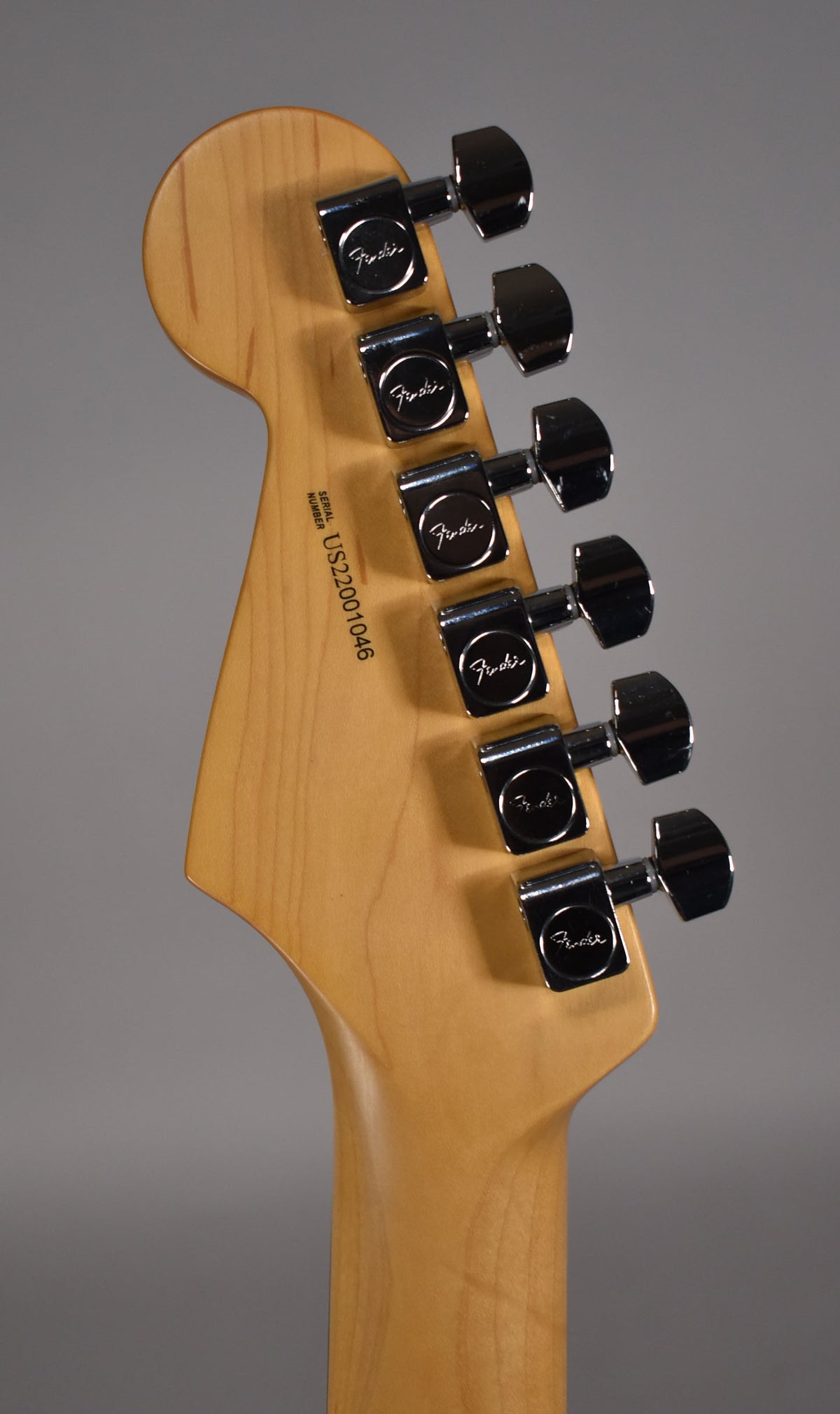The back of a light wood headstock and neck, showing six chrome tuners and a visible serial number.