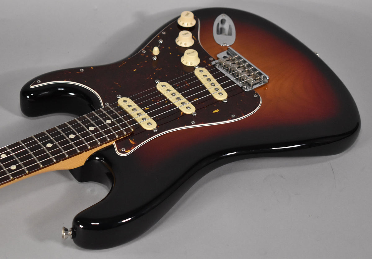 Sunburst Stratocaster body, angled from the lower bout, showing a tortoiseshell pickguard, three cream single-coil pickups, and chrome hardware.