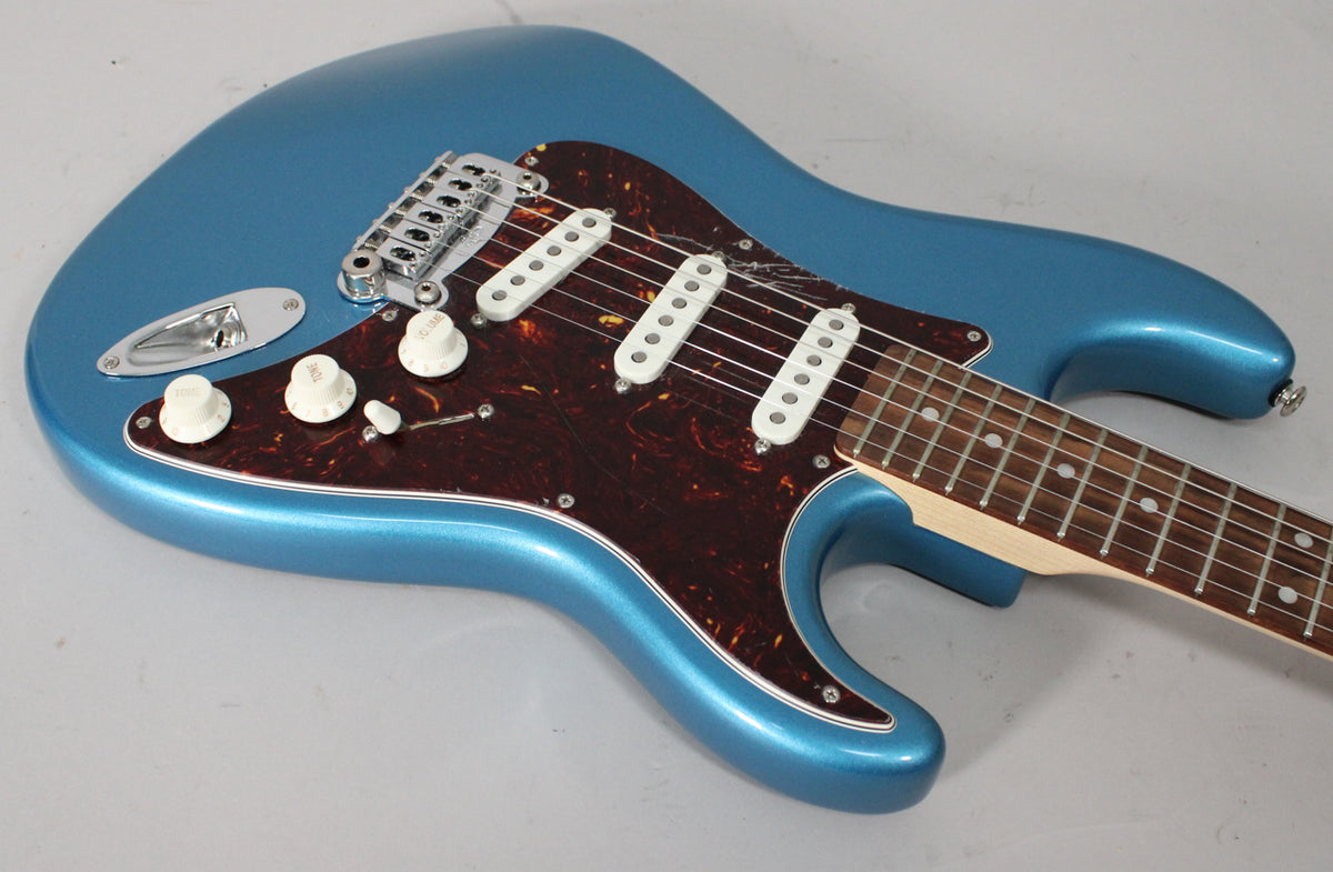 The metallic blue guitar body is angled, showing the tortoiseshell pickguard, three white single-coil pickups, and white control knobs.