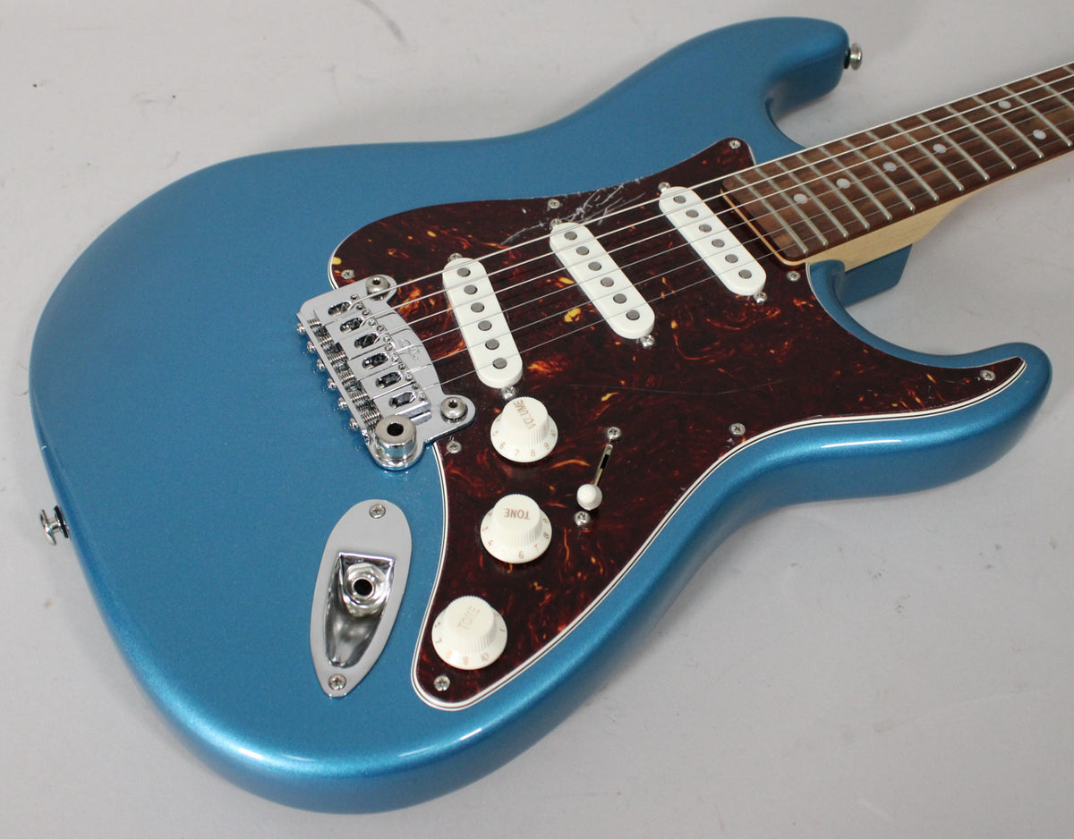 The metallic blue electric guitar's body is angled from the lower left, showing its tortoiseshell pickguard, three white pickups, and chrome bridge.
