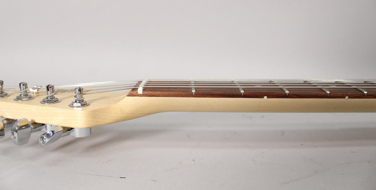 The guitar's light wood headstock and neck are seen from the side, with chrome tuners and a dark fretboard with white dot inlays.