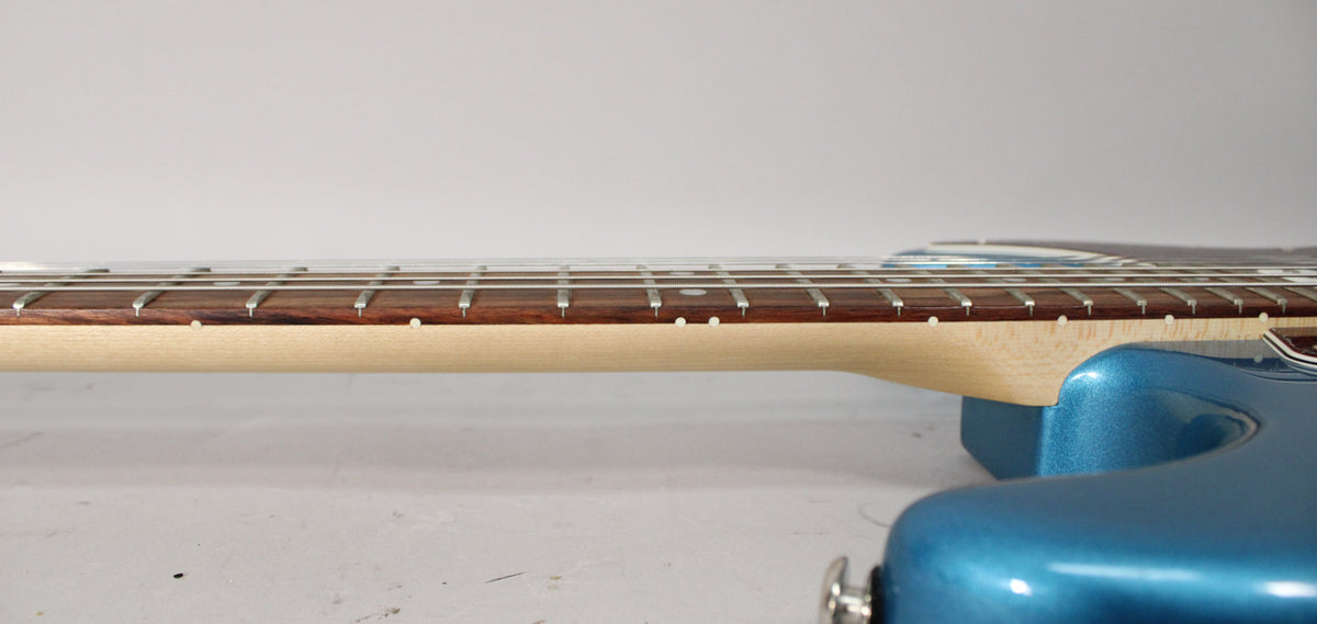 The guitar's light maple neck and dark rosewood fretboard with white dot inlays are visible from the side, joining a metallic blue body.