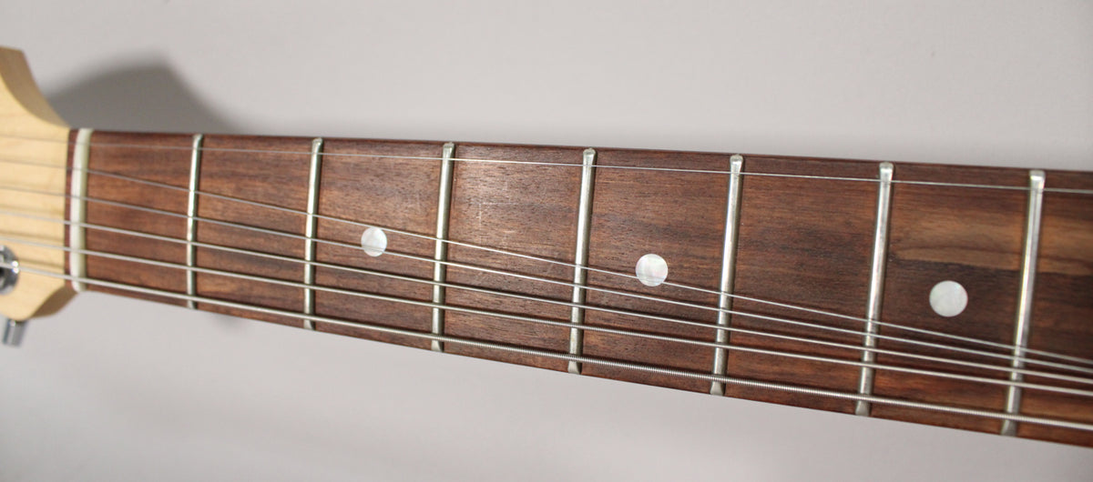 Close-up of the guitar's dark brown fretboard with six strings, silver frets, and three white dot inlays.