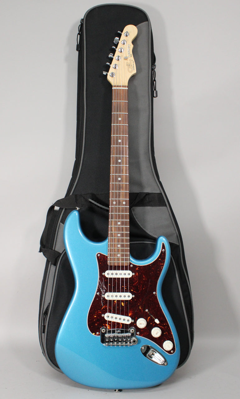 Full-length view of a metallic blue electric guitar with a tortoiseshell pickguard, white pickups, and a gig bag behind it.