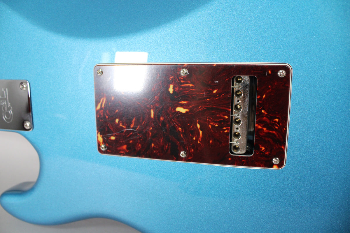 Close-up of the guitar's metallic blue back, showing a tortoiseshell tremolo cavity cover with six string holes and light surface scratches.