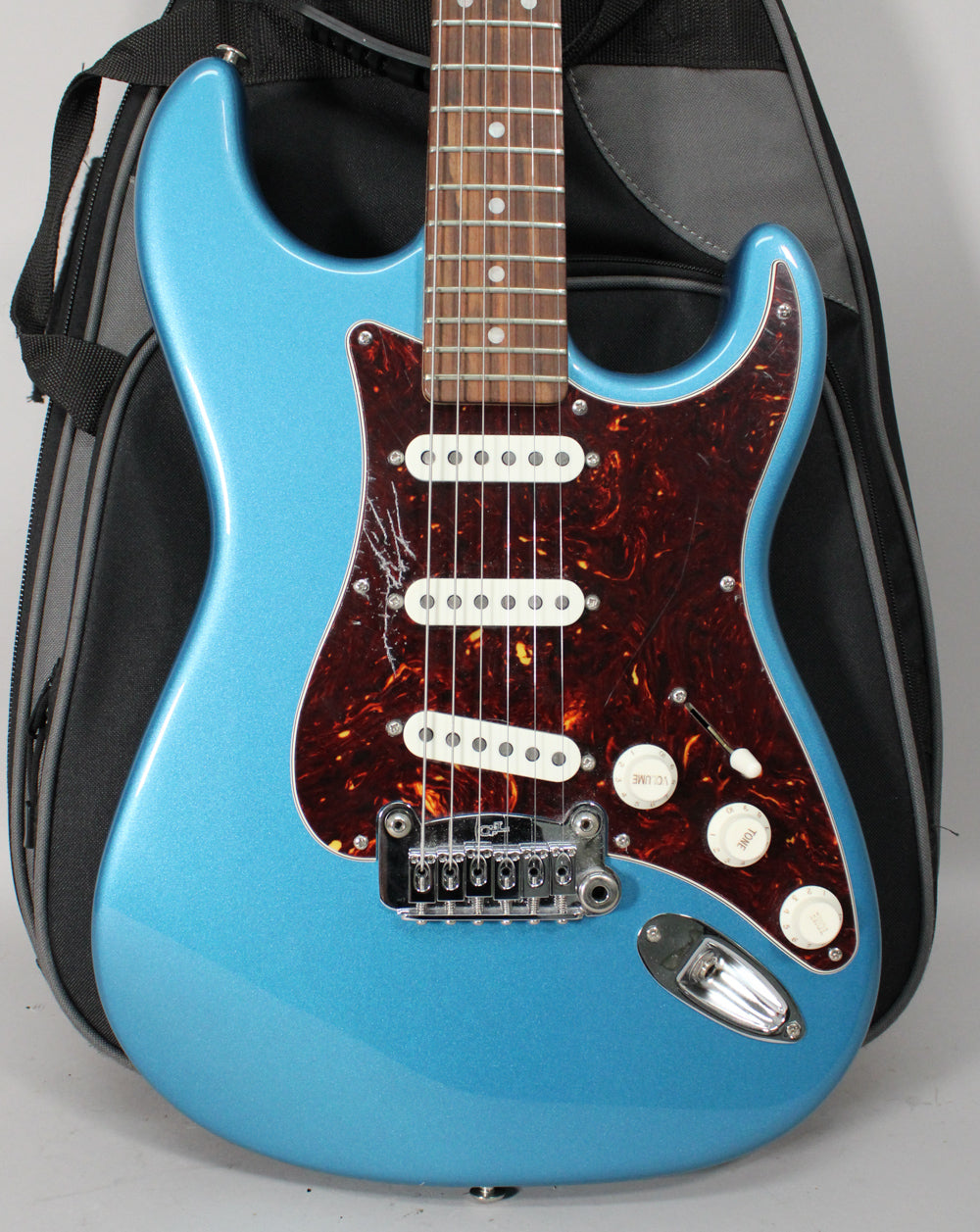 Lake Placid Blue metallic guitar, body and neck visible, with a tortoiseshell pickguard, three white single-coil pickups, and white knobs.