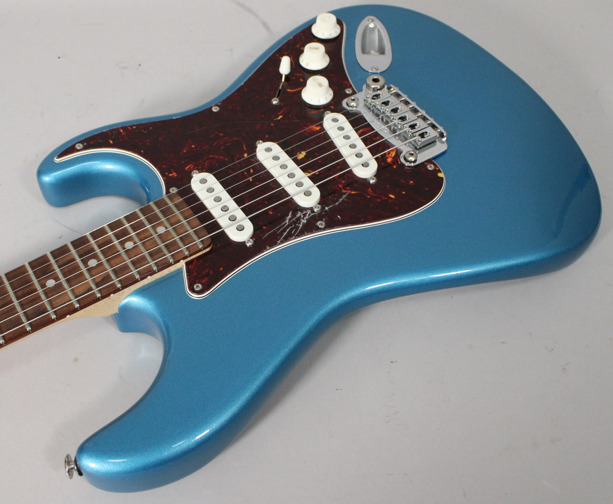 The metallic blue electric guitar is angled from above, showing its body, tortoiseshell pickguard, three white single-coil pickups, and chrome tremolo bridge.