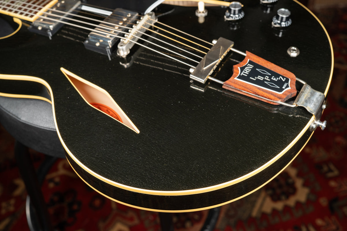 Close-up of the guitar's lower bout, showing the black body with heavy finish checking, f-hole, and a wooden trapeze tailpiece.