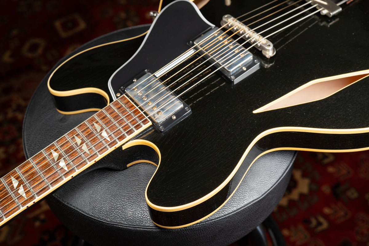 Close-up of the black semi-hollow body, showing the f-hole, two humbuckers, and the fretboard with split parallelogram inlays.