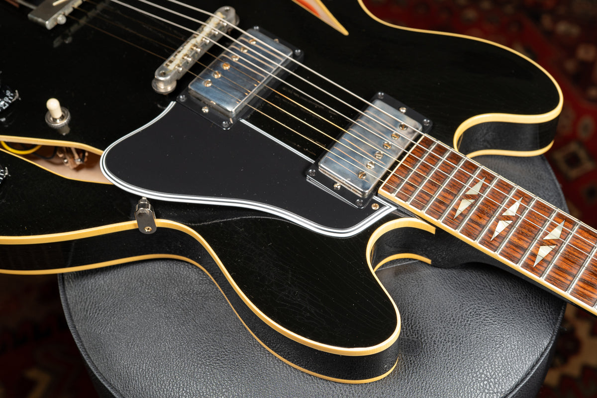 Close-up of a black semi-hollow guitar with a black pickguard, two humbuckers, and lightning bolt fretboard inlays.