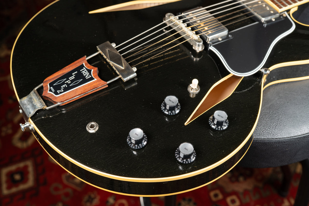 Close-up of the black guitar body, showing the tailpiece, four black control knobs, pickup selector, and f-holes.