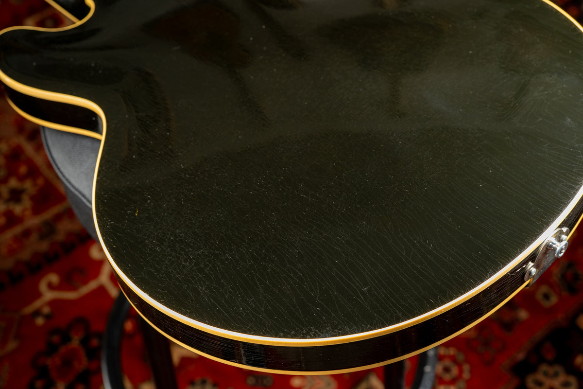 The guitar's black body, with visible finish checking and light wear, is framed from the upper bout to the lower bout.