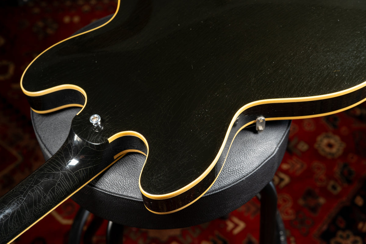 The guitar's black body and neck show extensive finish checking, with cream binding along the edges and a visible strap button.