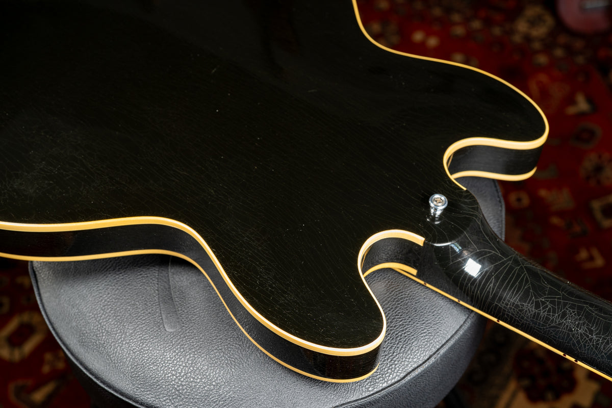The guitar's black body and neck show extensive finish checking, with cream binding visible along the cutaways and body edge.