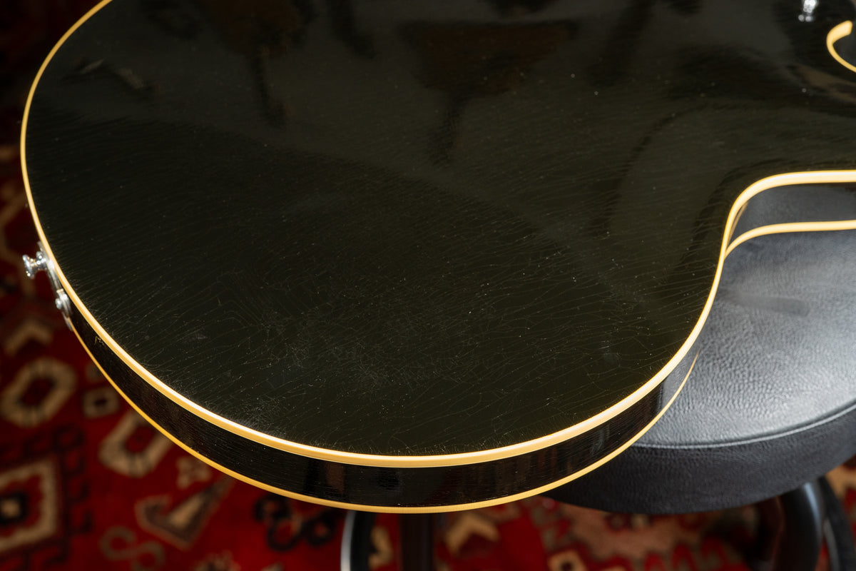 Close-up of the guitar's lower bout, showing the ebony finish with extensive fine checking and cream binding.