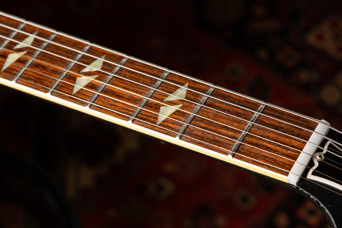 Close-up of the guitar's dark rosewood fretboard with trapezoid mother-of-pearl inlays, white binding, and a white nut.