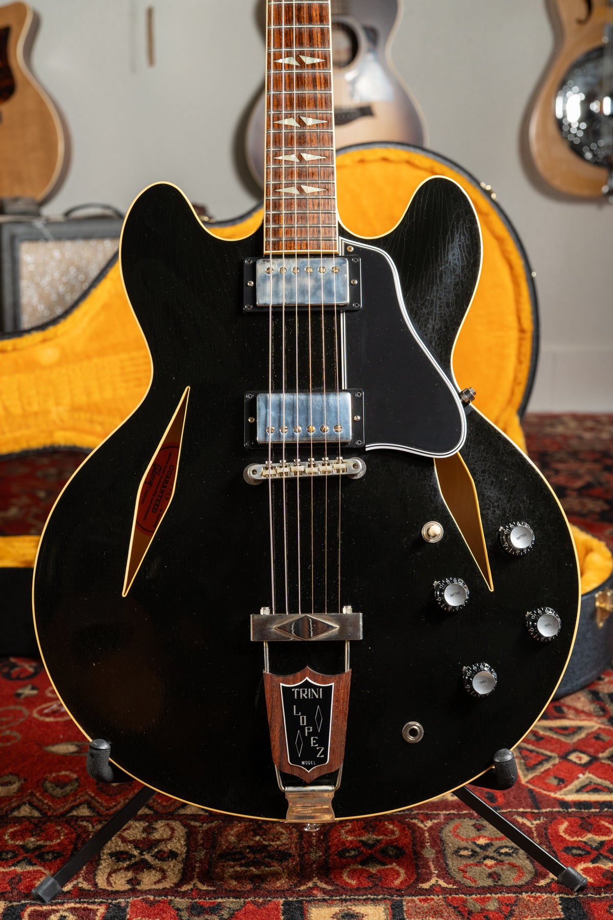 Full-frame view of a black semi-hollowbody electric guitar with a dark fretboard, trapezoid inlays, and a wooden trapeze tailpiece.