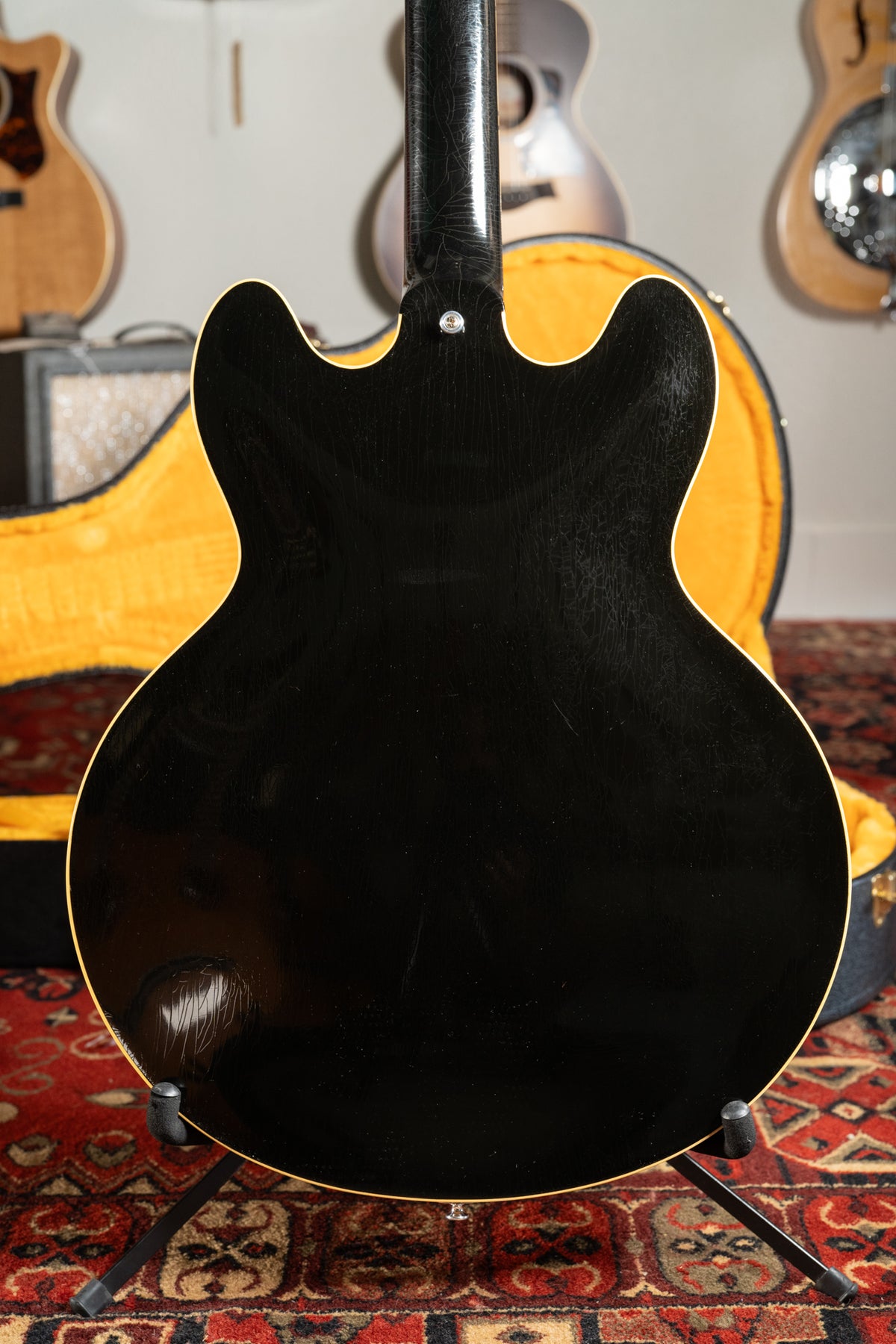 The back of a black semi-hollow electric guitar, showing finish checking and wear, with a yellow-lined case behind it.