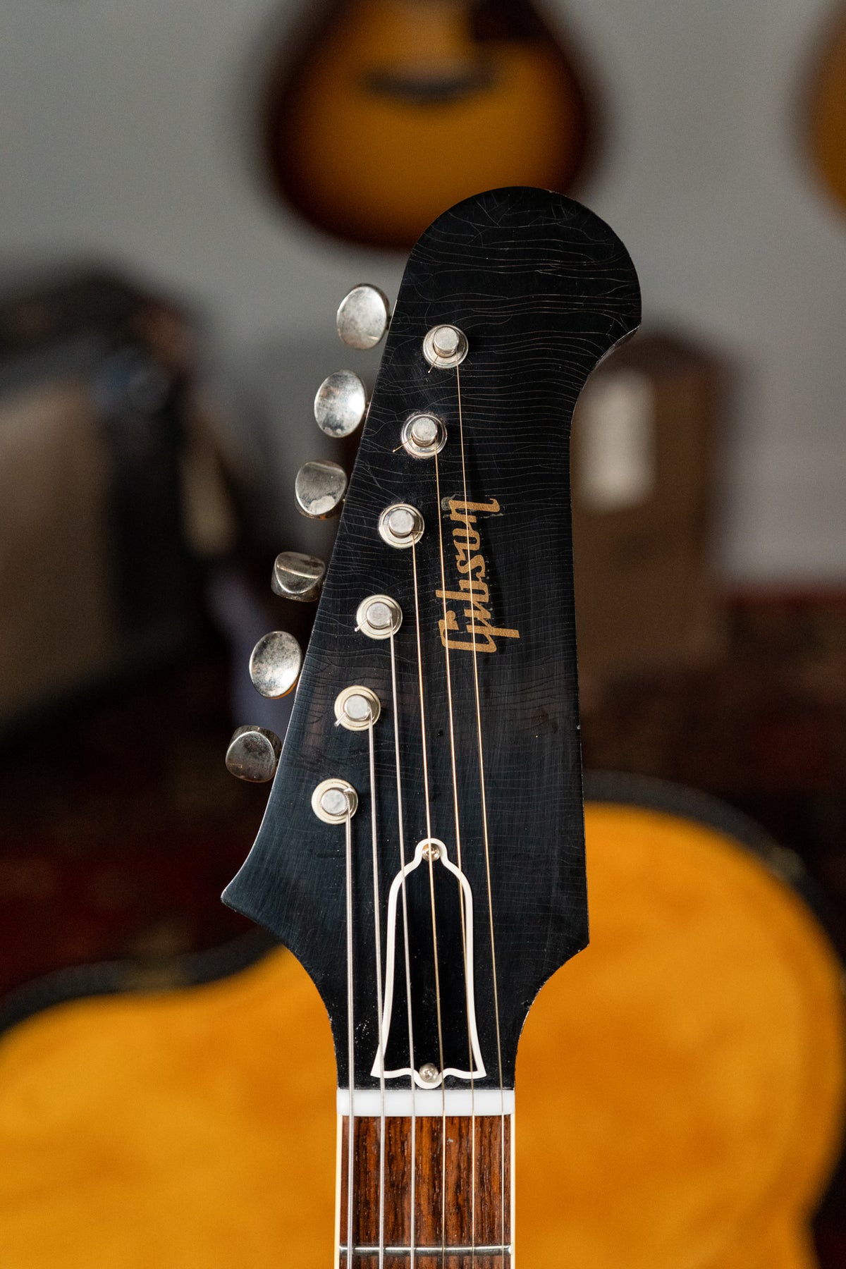 Close-up of the black headstock with gold Gibson script, six silver tuners, and a white bell-shaped truss rod cover.